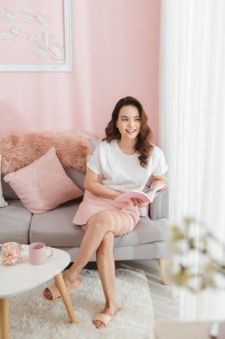 Gri kanepede kitap okuyan güzel bir kız.