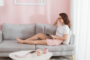 Ev, teknoloji ve internet kavramı - gülümseyen Asyalı kadın evinde dizüstü bilgisayarla kanepede yatıyor