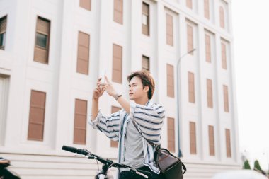 Havalı bir adam dışarıda bisiklet sürerken cep telefonu kullanırken sohbet ediyor. Ekose gömlek, tişört ve kot pantolon giymişti. Yakın plan..