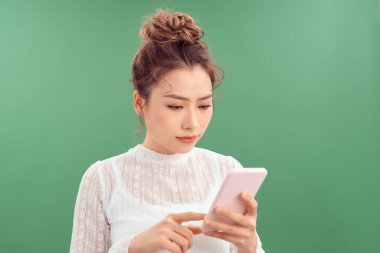 Kafası karışmış genç Asyalı kadın yeşil arka planda dururken akıllı telefon kullanıyor..