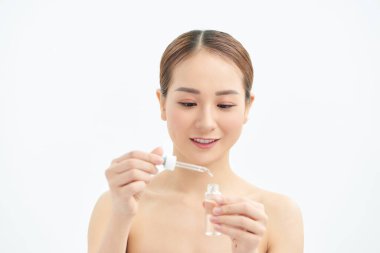 Yüzüne serum ya da cilt bakım ürünü süren Asyalı genç bir kız. Beyaz arkaplanda izole.