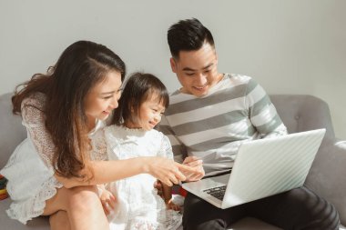 Young Family evdeki kanepede otururken dizüstü bilgisayar kullanıyor..