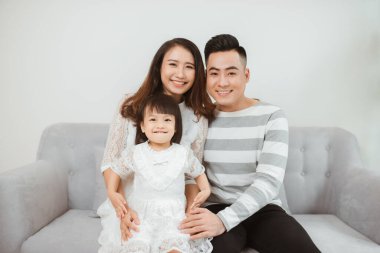 Mutlu, genç Asyalı bir aile kanepede oturuyor ve eğleniyor..