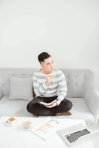 Young Asian Man Thinking Ideas Writing While Sitting Sofa Home — Stock Photo, Image