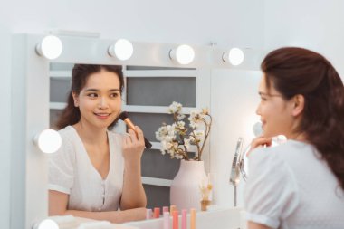 Genç ve güzel bir kadın aynanın yanında makyaj yapıyor.