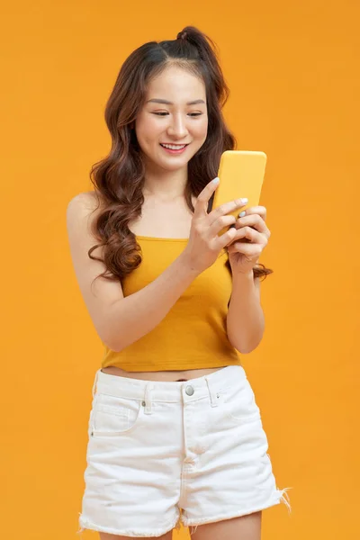 照片上一个笑容可亲的亚洲女人拿着手机站在黄色的背景上 — 图库照片