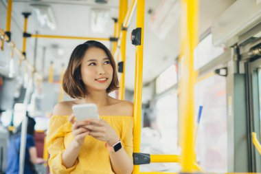 Telefon kullanan ve otobüs / toplu taşımada duran Asyalı genç kadının portresi.