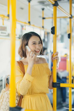 Genç Asyalı çekici kadın otobüste duruyor ve telefon kullanıyor..