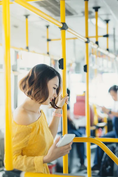 Attractive young Asian woman using phone when standing on the bus.