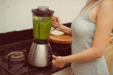 Mutfaktaki blender eviyle yeşil smoothie karıştıran sebzeli kadın.