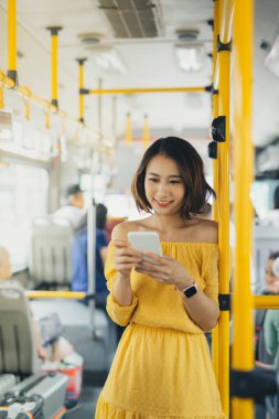 Otobüste / toplu taşımada dururken cep telefonu kullanan çekici genç bir kadın..