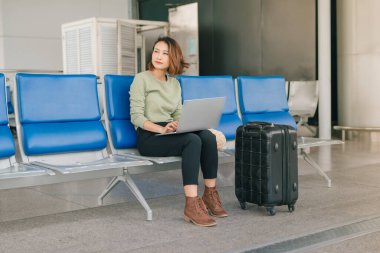 Genç Asyalı iş kadını dizüstü bilgisayar kullanıyor ve havaalanında otururken.... 