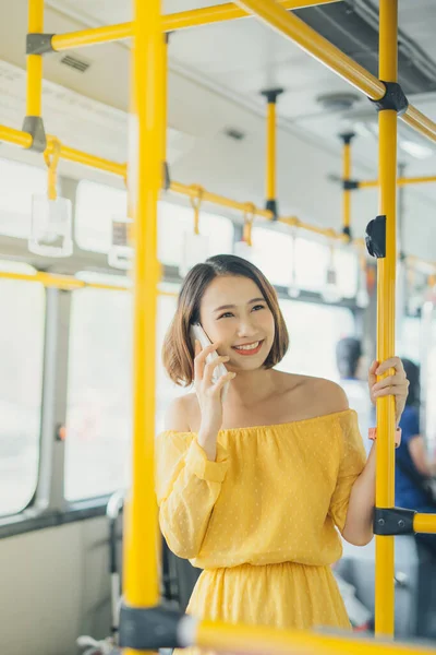 Portrait of young Asian woman using phone and standing on the bus/ public transportation.