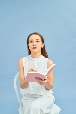 Sandalyeye oturmuş günce yazan gülümseyen güzel kız. 