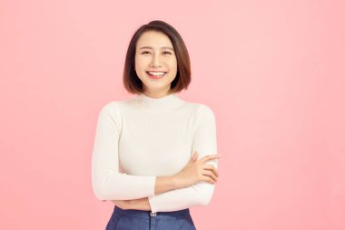 Soyutlanmış pembe arka plan üzerinde duran genç Asyalı kadın kollarını kavuşturup kameraya bakarken gülümsüyor. Pozitif kişi.
