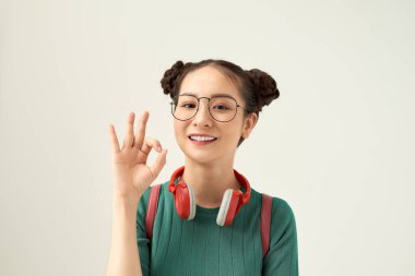 Ev ödevi kolaydır! Tatlı ve sevimli okuyucu kız, beyaz arka planda izole edilmiş sırt çantasıyla el yazısı gösteriyor.