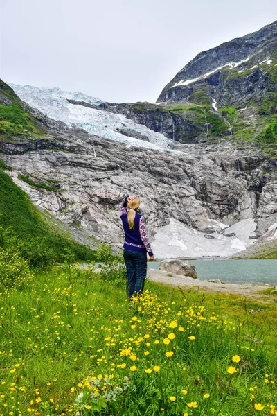 The young girl looks at the Boyabreen glacier. Melting glacier forms the lake with clear water. Norway. — Stock Photo, Image