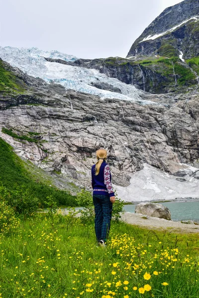 The young girl looks at the Boyabreen glacier. Melting glacier forms the lake with clear water. Norway. — Stock Photo, Image