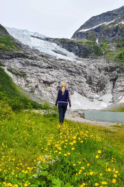 The young girl looks at the Boyabreen glacier. Melting glacier forms the lake with clear water. Norway. — Stock Photo, Image