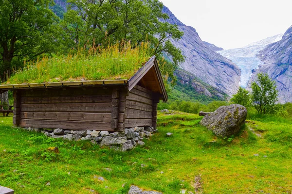Case tradizionali con erba verde sul tetto sullo sfondo del ghiacciaio Briksdalsbreen . — Foto Stock