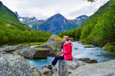 Briksdalsbreen (Briksdal) buzuluna yakın nehir kenarında bulunan genç kadın. Bu buzulun erimesi temiz suyla şelale ve nehri oluşturur. Jostedalsbreen Ulusal Parkı. Norveç.