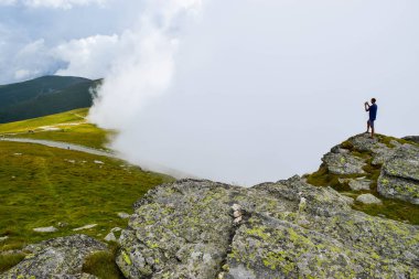 Adam, Transalpina yolu yakınlarında sis ve alçak bulutlarla çevrili olarak tepede duruyor. Burası Romanya 'nın en güzel dağlık yolları ve en yüksek asfalt yollarından biri..