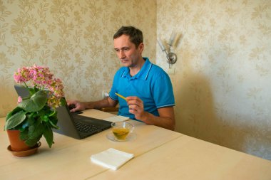 Genç adam evden çıkmadan bilgisayarın başında uzaktan çalışıyor. Karantina döneminde evden uzak çalışma ve kendini izole etme.