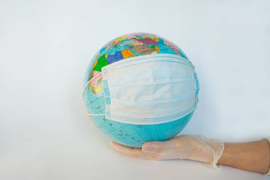 Koruyucu eldiven giymiş bir adamın elinde koruyucu maske takmış bir dünya küresi. Tüm gezegendeki insanların Coronavirus salgını ve salgını nedeniyle karantinaya alındığının sembolü. Beyaz arkaplan.