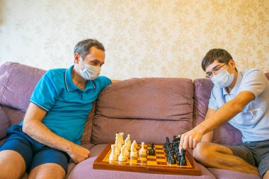 Korumalı maskeli baba ve genç oğul satranç oynuyorlar, Coronavirus salgını ve salgını sırasında kendi başlarına karantinada kalıyorlar..