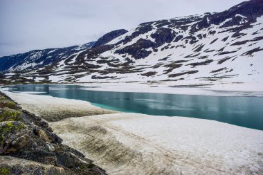 Eriyen kardan oluşan göl ile dağ manzarası. Küresel ısınma ve iklim değişikliği, kar örtüsünü ve buzulları azaltıyor.