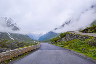 Beautiful narrow road in the mountains covered by fog and low clouds. National tourist road 258 Stryn - Grotu, that running across the mountains. Trip by car to Norway. clipart