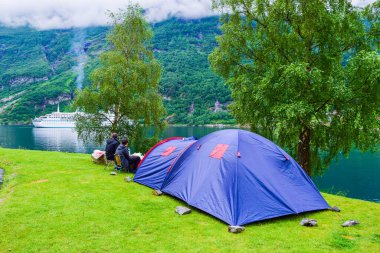 Geirangerfjord kıyısındaki Geiranger yakınlarında yolcu gemisinin arka planında bulunan mavi turist çadırı, Geiranger adlı küçük bir köye giriyor. Norveç 'e yaz yolculuğu.