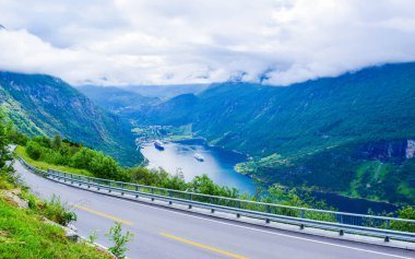 Geirangerfjord 'un sonundaki yolcu gemileri Geiranger köyünün yakınlarında. Eagles Yolu 'ndan görüntü. Bulutlu havada fiyort ve dağların manzarası. Norveç 'e yaz yolculuğu macerası.