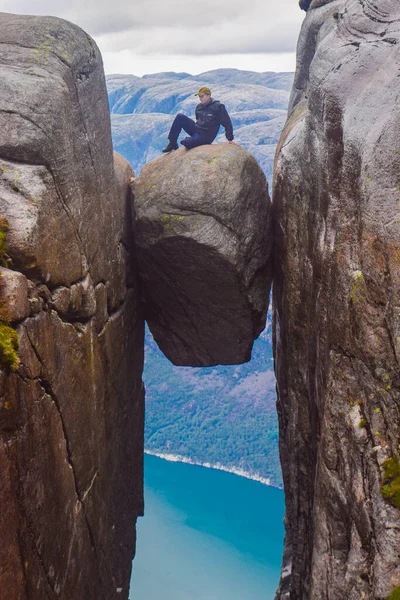 这位观光客坐在世界上最危险的石头Kjeragbolten顶上 Kjeragbolten是位于挪威Kjerag山上Lysefjorden上空984米的岩石 — 图库照片