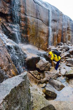 Turist, Kjeragbolten yakınlarındaki uçurumlardan düşen bir şelaleden su içiyor. Lysefjorden 'ın 984 metre yüksekliğinde sıkışmış dünyanın en tehlikeli taşı. Norveç.
