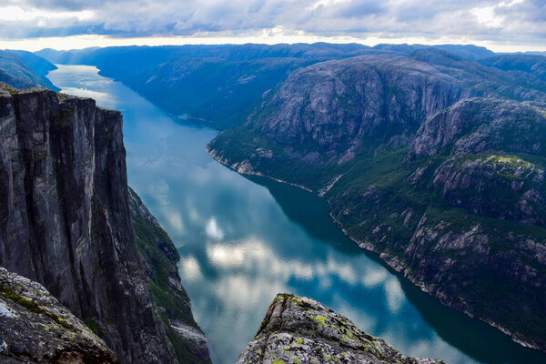 Прекрасный горный пейзаж Люсе-фьорда с облаками, отраженными в голубой воде. Вид с плато Кьяраг, где недалеко на высоте 984 метра застрял между двумя скалами Керагболтена. Норвегия
.