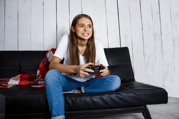 Beautiful girl playing video games, sitting on sofa at home.