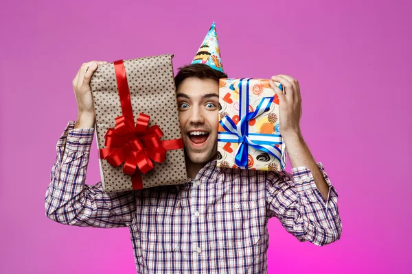 Happy man holding birthday gifts in boxes over purple background.