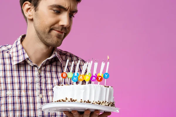 Displeased man holding birthday cake with one not blow out candle.