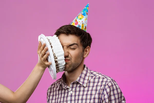 Man with cake on face over purple background. Birthday party.