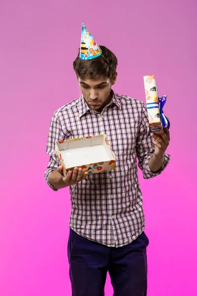 Young handsome man opening birthday gift over purple background.