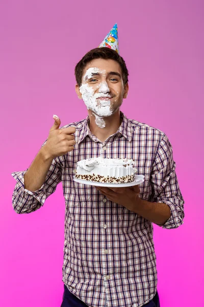 Man with cake on face over purple background. Birthday party.