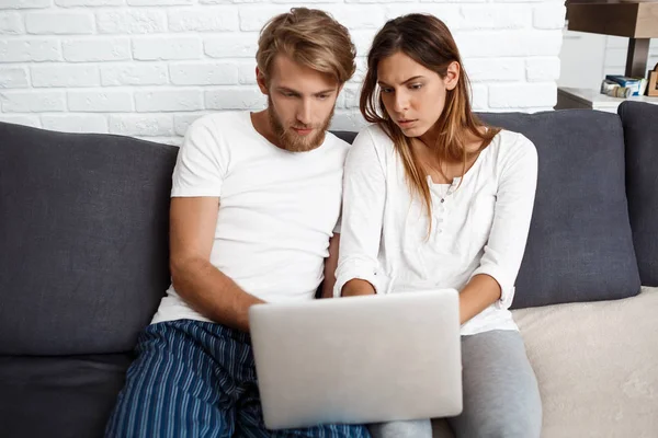 Beautiful couple looking at laptop sitting on sofa  home.
