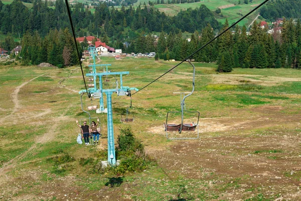 Young couple going up on ski lift, Carpathian mountains background.
