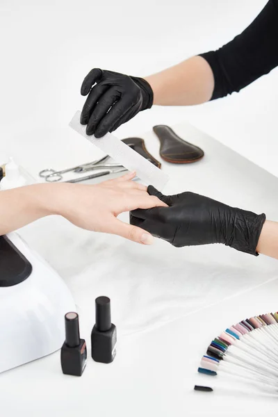 Nail artist working with nail file making manicure at salon.