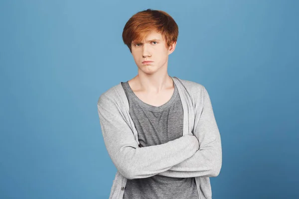 Close up of unhappy young good-looking ginger boy in casual stylish outfit crossing hands, looking in camera with offended and unsatisfied face expression, after argument with girlfriend.