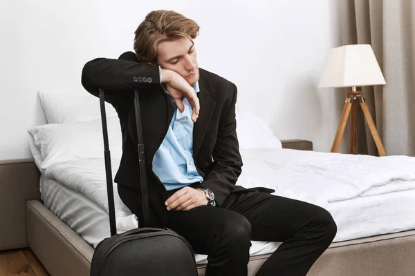 Young handsome businessman in black suit fall asleep with suitcase in hotel room after long trip in plane on business mission.