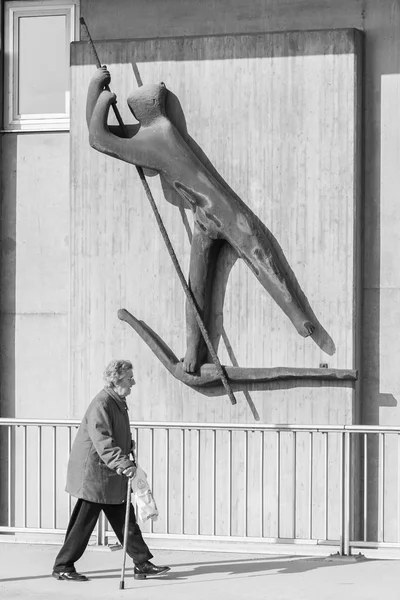 Germany, Regensburg, March 17, 2017, Street photography of an old woman under a ferryman sculpture in regensburg — Stock Photo, Image