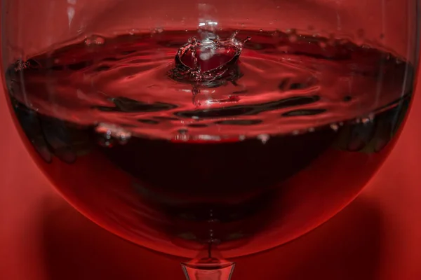 Rotweintropfen in einem Rotweinglas und Wellen mit rotem Hintergrund und Spiegelung — Stockfoto