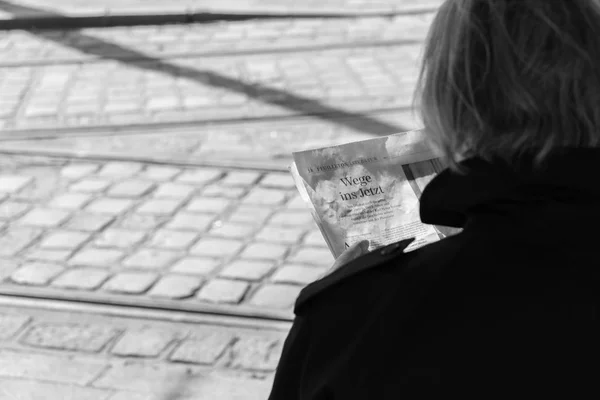 Alemania, Múnich, 25 de marzo de 2017, Vista sobre el hombro de una mujer mayor leyendo un periódico sobre cómo entrar ahora y algunas carreteras ferroviarias en el fondo — Foto de Stock